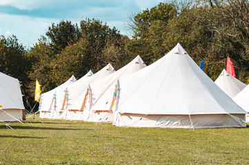 Light creme canvas waterproof tent in a green field on a nice and hot summer day. Blue Clouds, green grass, Child festival tent.