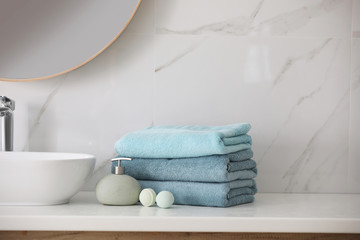 Stack of fresh towels, soap dispenser and bath bombs on countertop  indoors