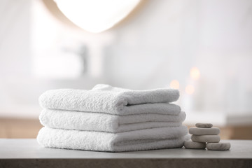 Stack of fresh towels and spa stones on table in bathroom