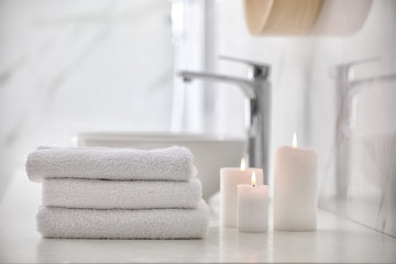 Stack of fresh towels and burning candles on countertop in bathroom