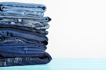Stack of different jeans on blue wooden table. Space for text