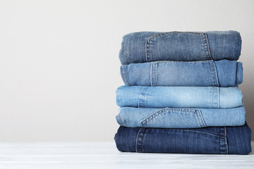 Stack of different jeans on white wooden table. Space for text