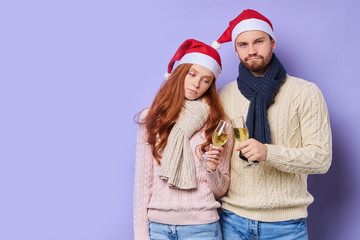 Pretty sad redhead woman wearing Santa's hat, trying to clink glass of champagne, looking down with tired face, expressing disappointment, having bothering evening, Christmas concept