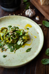 Delicious homemade pasta pappardelle with squid, freshmade pesto sauce, olive oil and pine nuts on a brown wooden table in a pasta bar.