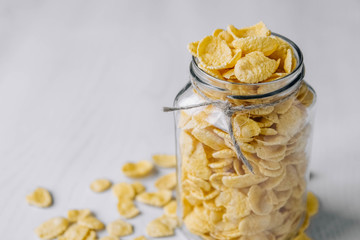 Corn flakes in a glass jar on white wooden surface. Top view. Place for your text