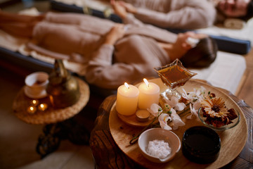 Caucasian male and female at spa procedures relax and drink tea while lying down in special beds in spa salon, wearing bathrobes, around candles