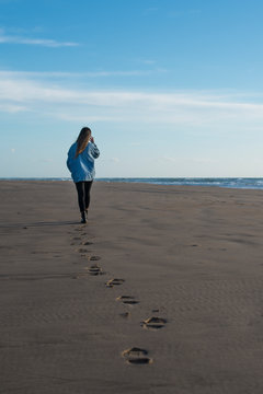 chica joven de espaldas paseando en la playa dejando sus huellas en la arena