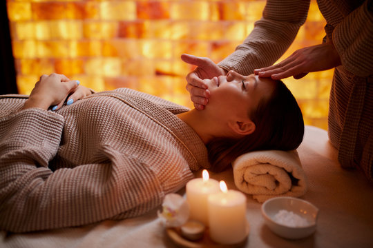 Young Caucasian Lady Get Reacreation Massage Of Head, Face. Lying Down On Desk For Massages Wearing Bathrobe