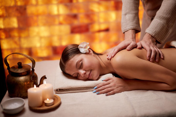 Obraz na płótnie Canvas Attractive young female get massage on back lying on table in spa salon, naked back. female hands doing massage, using candles