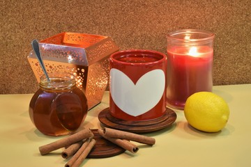 Hot tea in a red cup with a painted white heart on it and with cinnamon, honey and lemon.
