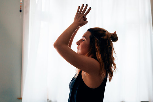 close up of a woman in a yoga position with closed eyes, clasped hands and raised arms performing the sun salutation flow - healthy lifestyle and meditation concept