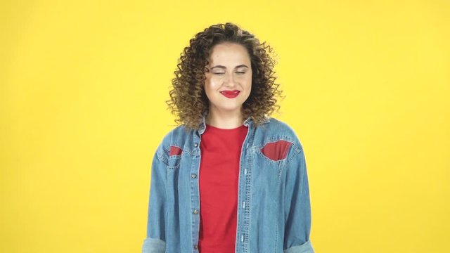 Curly girl coquettishly smiles while looking at the camera, builds her eyes, slow motion