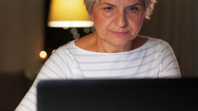 technology, old age and people concept - senior woman with laptop at home in evening