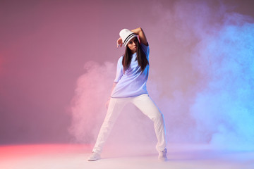 Young pretty hip hop dancer dressed in white pants, blue t shirt with cap dancing on stage full of...