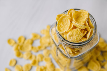 Corn flakes in a glass jar on white wooden surface. Top view. Place for your text