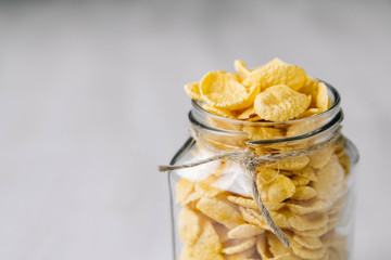 Corn flakes in a glass jar on white wooden surface. Place for your text