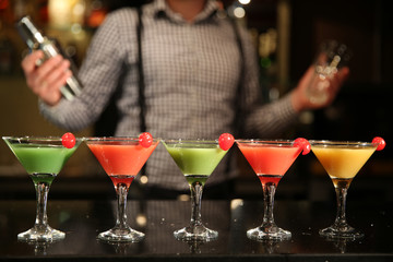 Multi-colored cocktails close-up. Barman with a shaker and five different cocktails on a black bar counter. Recreation entertainment. A selection of drinks at the bar at night.