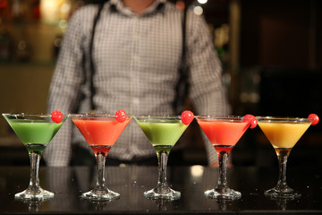 Multi-colored cocktails close-up. Barman with a shaker and five different cocktails on a black bar counter. Recreation entertainment. A selection of drinks at the bar at night.