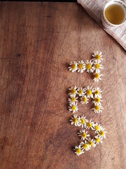 Word TEA written with chamomile flowers on a rustic table. Background 