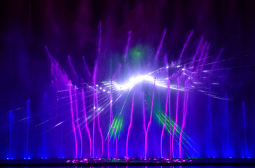 Colorful water fountains. Beautiful laser and fountains show. Large multi colored decorative dancing water jet led light fountain show at night. Dark background.