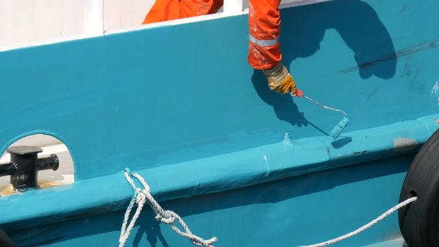 Hand of a man of a sailor paints with a paint with a roller stern of a ship or boat with blue paint