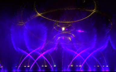 Colorful water fountains. Beautiful laser and fountains show. Large multi colored decorative dancing water jet led light fountain show at night. Dark background.