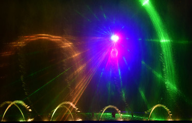 Colorful water fountains. Beautiful laser and fountains show. Large multi colored decorative dancing water jet led light fountain show at night. Dark background.