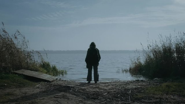 Young woman at the lake looking into the distance. Aerial, dolly shot.