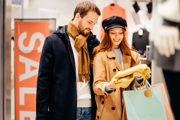 Young caucasian couple together want to buy new blouse for wife, clothes store in the background