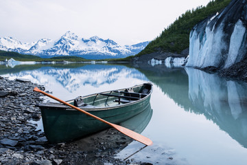 Canoe resting on rock covered ice of Valdez Glacier with icebergs behind. Valdez, Alaska. - obrazy, fototapety, plakaty