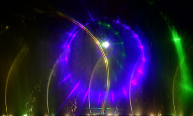 Fototapeta premium Colorful water fountains. Beautiful laser and fountains show. Large multi colored decorative dancing water jet led light fountain show at night. Dark background.