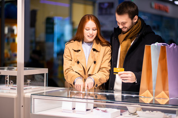 Fototapeta na wymiar beautiful lovely cute couple in shopping mall together, decided to buy jewelry for woman, man holding discount card in hands going to buy ring