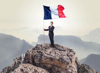 Obraz premium Successful businessman on the top of a mountain holding France victory flag
