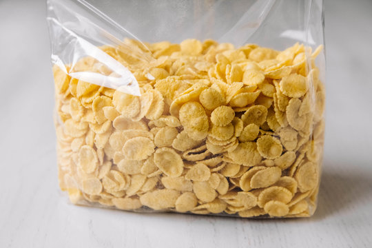 Cornflakes in plastic bag on white wooden surface. Place for your text