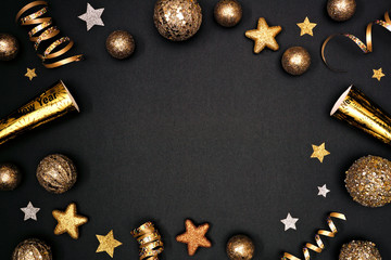 New Years Eve frame of glittery gold stars, streamers, decorations and noisemakers. Above view on a black background.