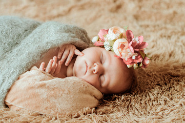 A newborn girl lies on a brown blanket. Wreath of flowers on his head. Brown fluffy plaid . The baby is fast asleep.
