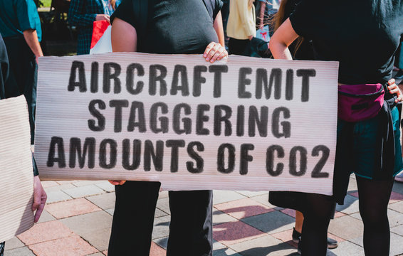 The phrase " Aircraft emit staggering amounts of CO2 " drawn on a carton banner. A girl holds a cardboard with an inscription. Girls on the street. Pollution. CO2