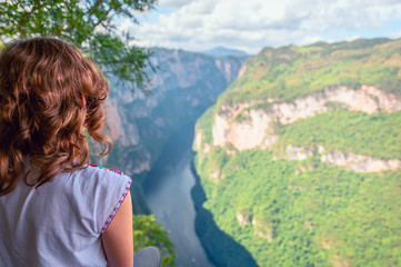Fototapeta na wymiar Young woman with typical Mexican blouse watching from the heights the Cañon Del Sumidero through which it crosses the Grijalva river, with monañas in the background and blue sky