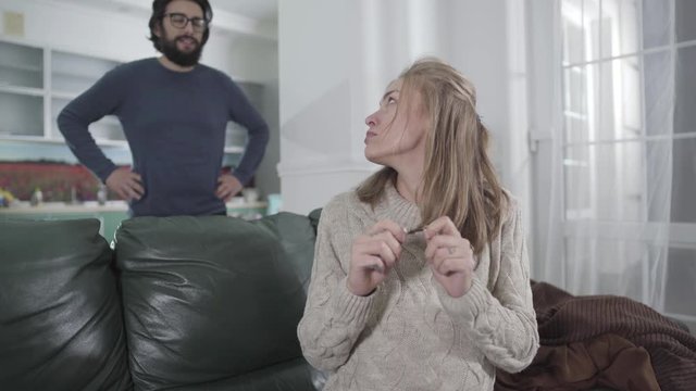 Young blond Caucasian woman breaking cigarette and looking back at her husband. Bearded man gesturing yes. Pregnant woman getting rid of bad habits. Pregnancy, healthy lifestyle.