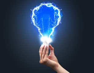 Hand holding shiny light bulb on dark background. New idea concept