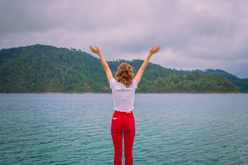 Young woman with arms raised, enjoying the freedom and the landscape of a turquoise blue lagoon