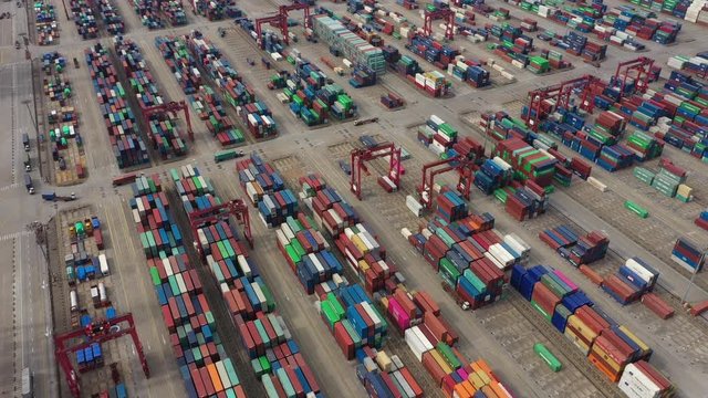 Tilted aerial view of cargo trucks driving through stacks of colorful containers in the Port of Shanghai facilities, economy and infrastructure in China