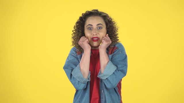 Very surprised girl with shocked wow face expression on yellow background at studio, slow motion.