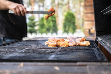Man puts chicken on the grill to prepare a family dinner in the courtyard of the house, on a sunny summer day. Barbecue in the backyard.
