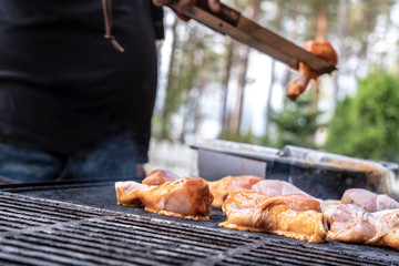 Man puts chicken on the grill to prepare a family dinner in the courtyard of the house, on a sunny summer day. Barbecue in the backyard.