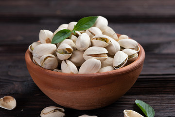  Pistachio in wooden bowl in background with green leaves.