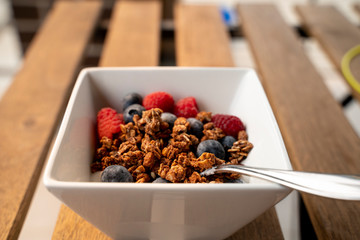 Yogurt with baked granola and berries in small bowl, raspberries, blueberries