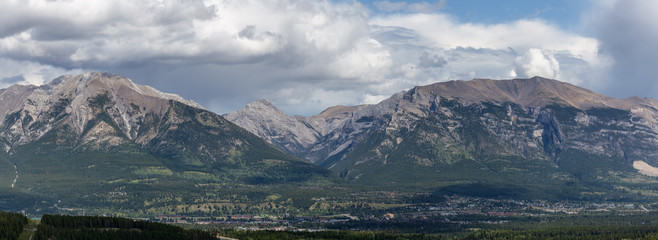 Beautiful Panoramic View of a small city in the Canadian Rocky Mountain Landscape during a cloudy summer day. Taken in Canmore, Alberta, Canada.