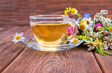 Herbal tea in a glass cup with bouquet of wild flowers on a wooden background. Text space.
