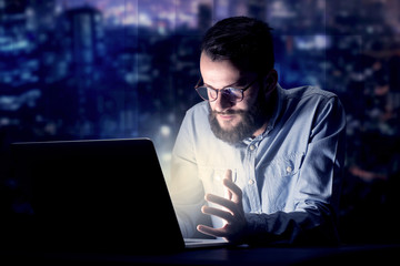 Young handsome businessman working late at night in the office with blue lights in the background